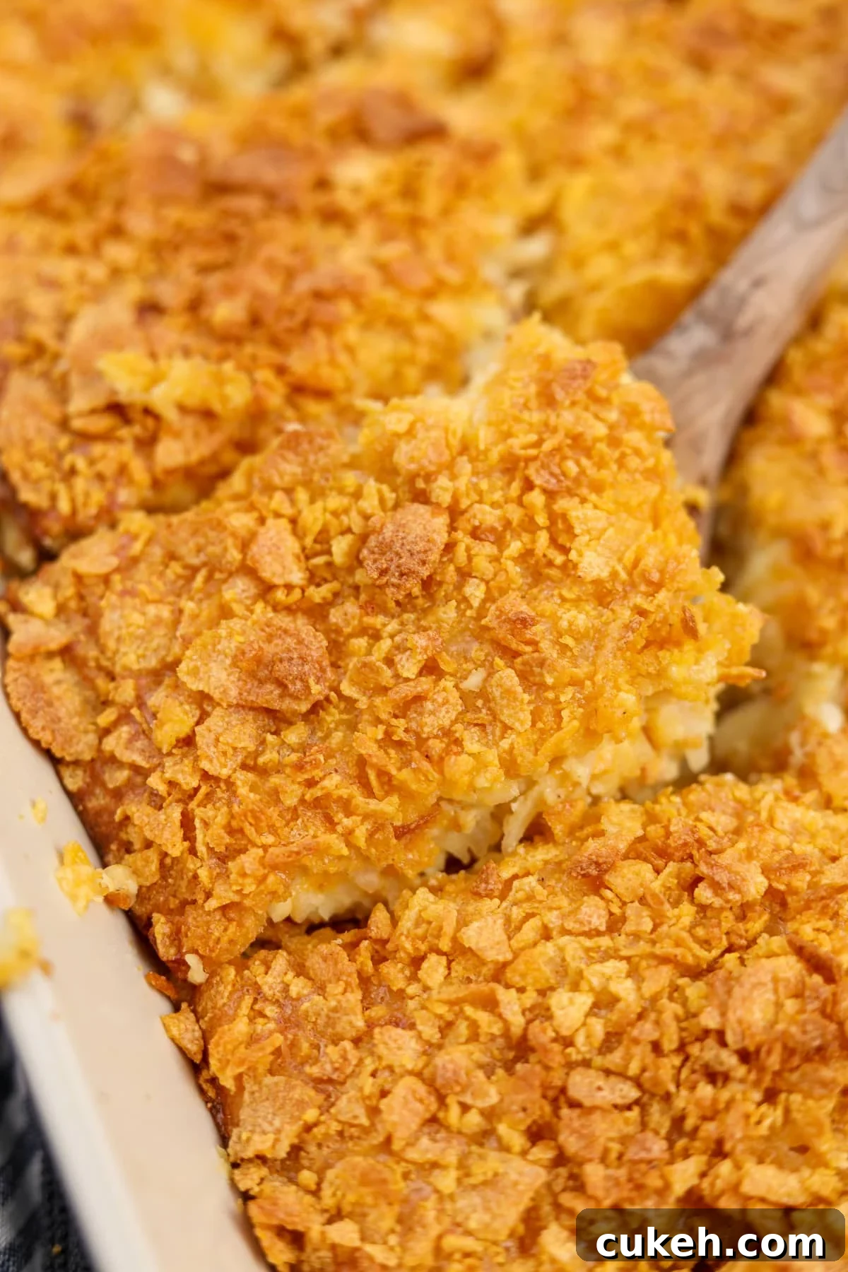 A wooden spatula serving up a square of breakfast casserole topped with crunchy cornflakes. 