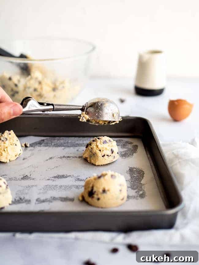 hand holding icecream scoop with chocolate chip cookies on a baking sheet