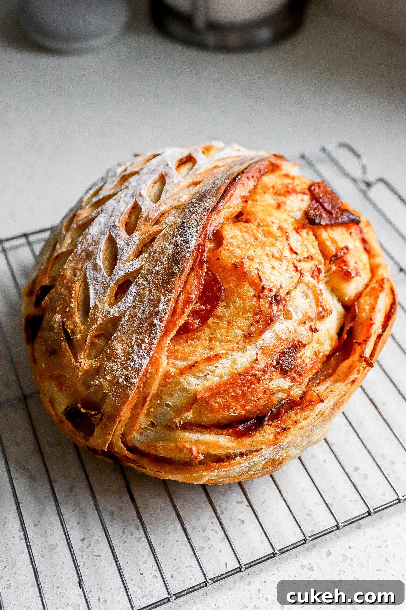 Side angle of pepperoni pizza sourdough bread on cooling rack with designs on the top of the loaf.
