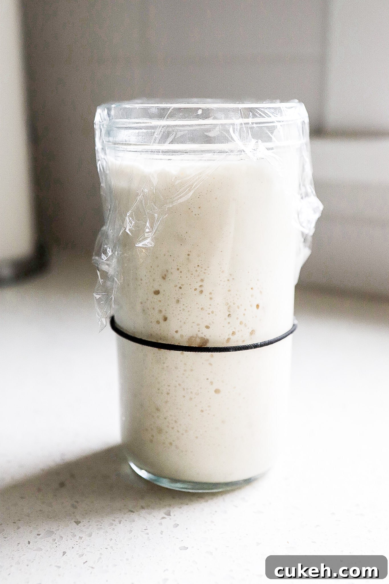 Side view of active sourdough starter in glass jar covered with plastic wrap.