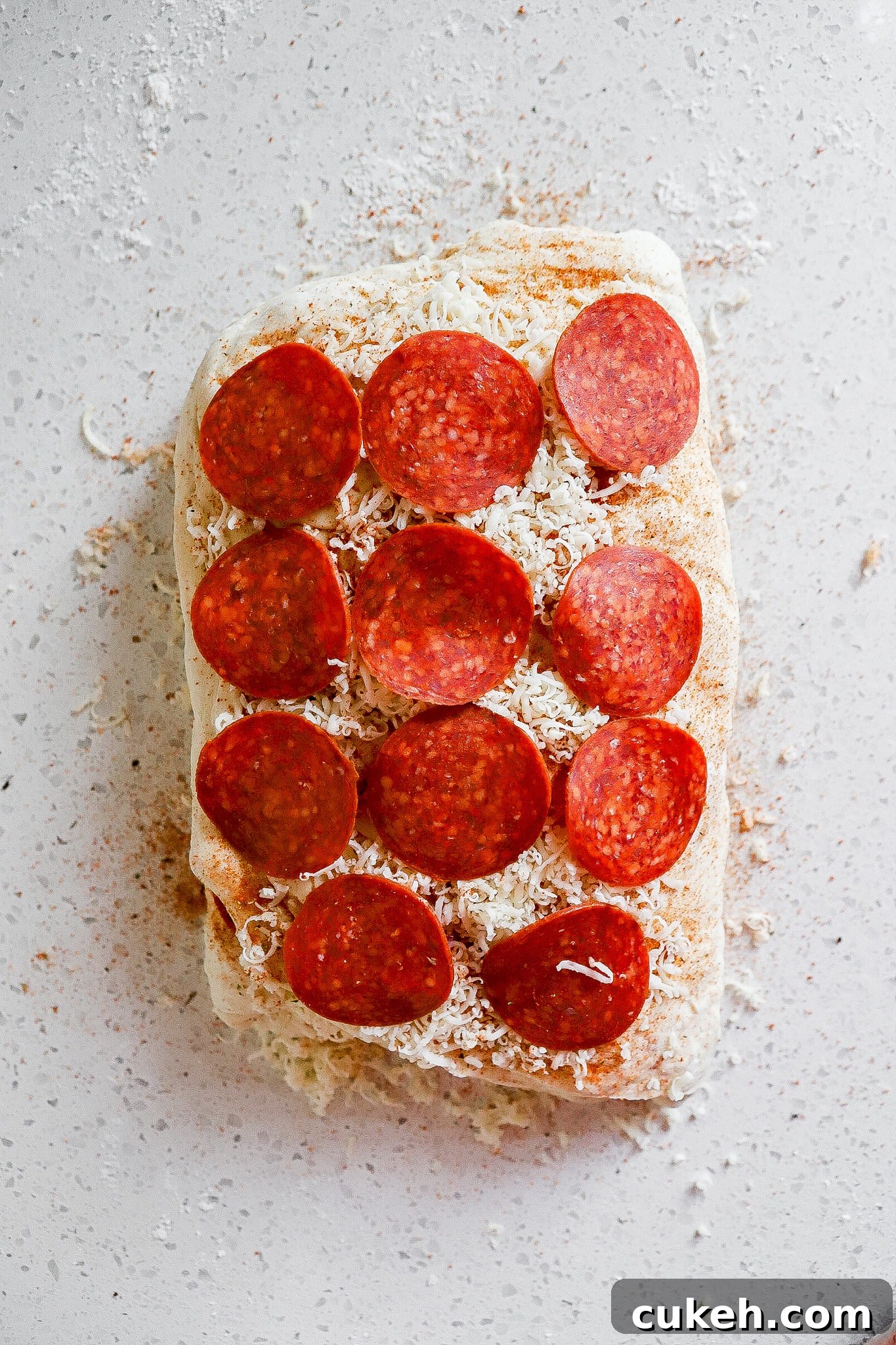 Top down view of pepperoni pieces on top of dough with shredded mozzarella cheese.