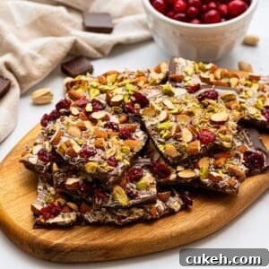 Chocolate bark on cutting board made with chopped nuts, dried cranberries, and sea salt.