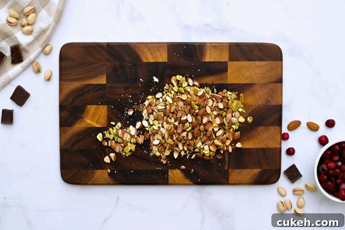 Toasted pistachios and almonds on cutting board chopped next to dark chocolate pieces.