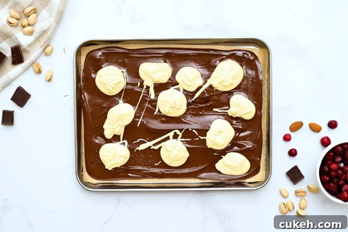 Melted white chocolate dolloped in spoonfuls over melted dark chocolate on parchment lined baking sheet.