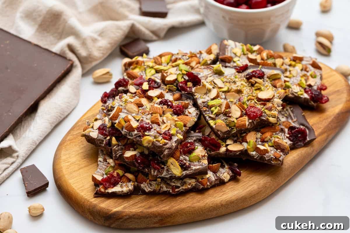 Chocolate bark broken into large chunks on cutting board made with chopped nuts, dried cranberries, and sea salt.
