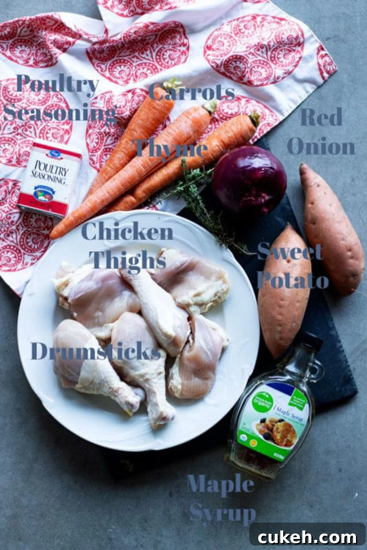 Chicken thighs and drumsticks, carrots, red onion, sweet potato, thyme, maple syrup, seasoning on table.