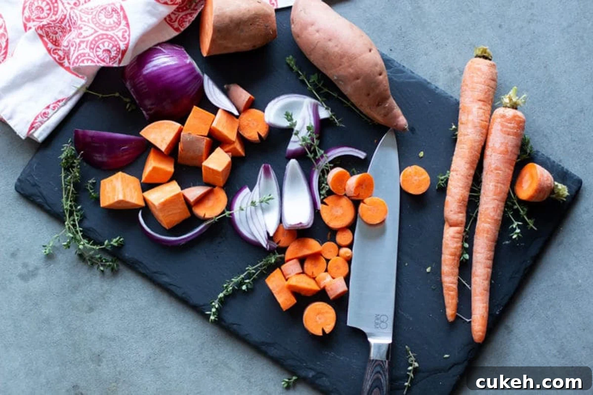 Black cutting board with chopped sweet potatoes, red onion, and carrots.