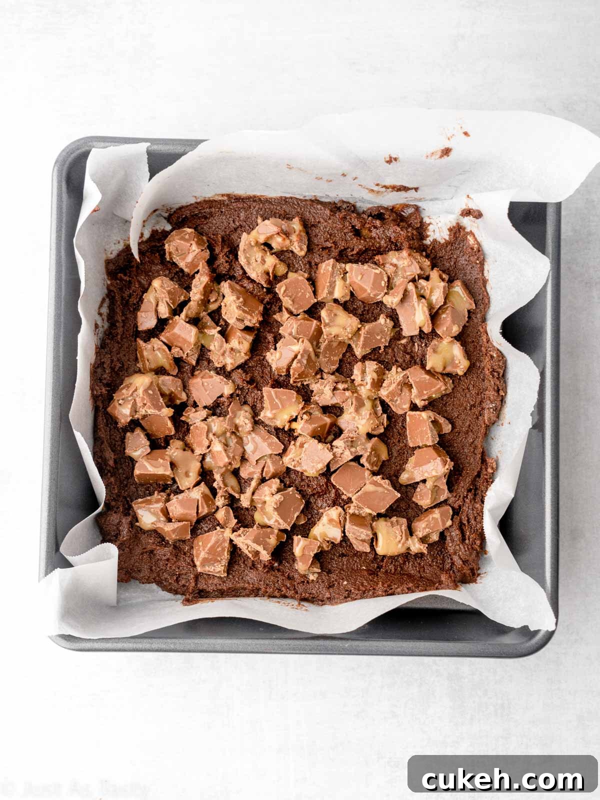 Brownie batter topped with chopped Rolos in a pan.