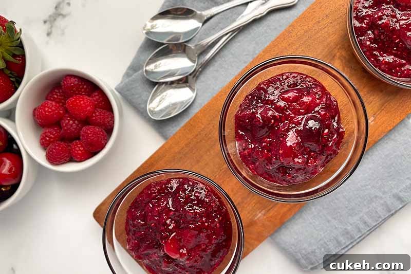 Horizontal image of three glass bowls filled with thick compote on a wooden plank next to silverware.