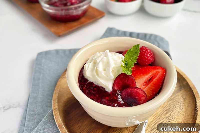 Horizontal image of a bowl filled with compote, whipped cream, and assorted fruit with a mint garnish.