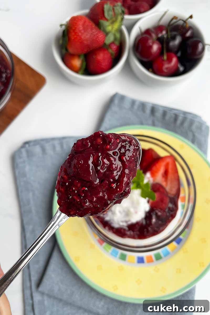Vertical image of a metal spoon holding a scoopful of a thick compote over a yellow plate on a blue napkin.