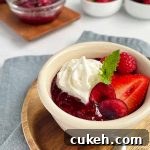 Horizontal image of a bowl filled with compote, whipped cream, and assorted fruit with a mint garnish.