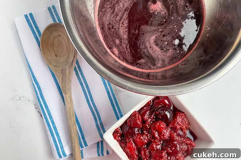 Horizontal image of a large metal bowl filled with a deep maroon liquid next to stewed fruit.