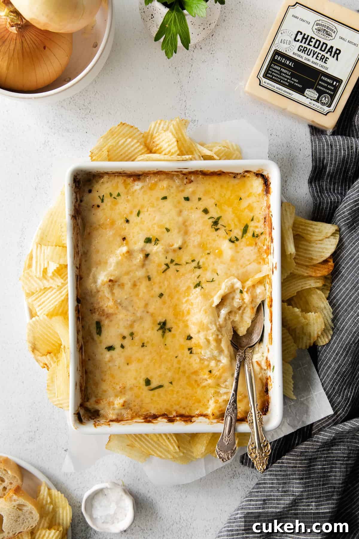This French Onion Dip is made deliciously cheesy with help from cheddar gruyere and cream cheese. Enjoy this dip as an appetizer or savory snack! French onion dip in a casserole dish surrounded by potato chips.