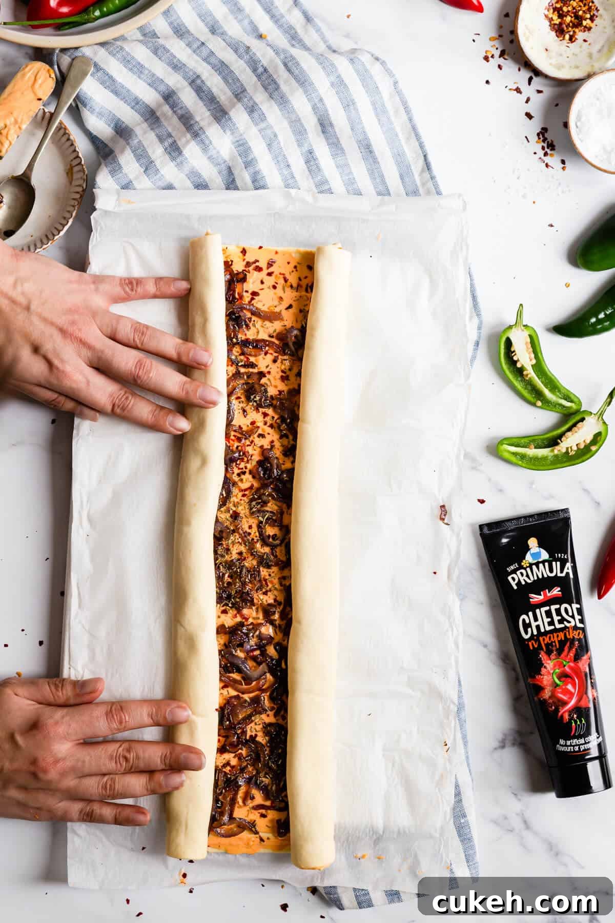 top view of person rolling side of puff pastry sheet towards the middle