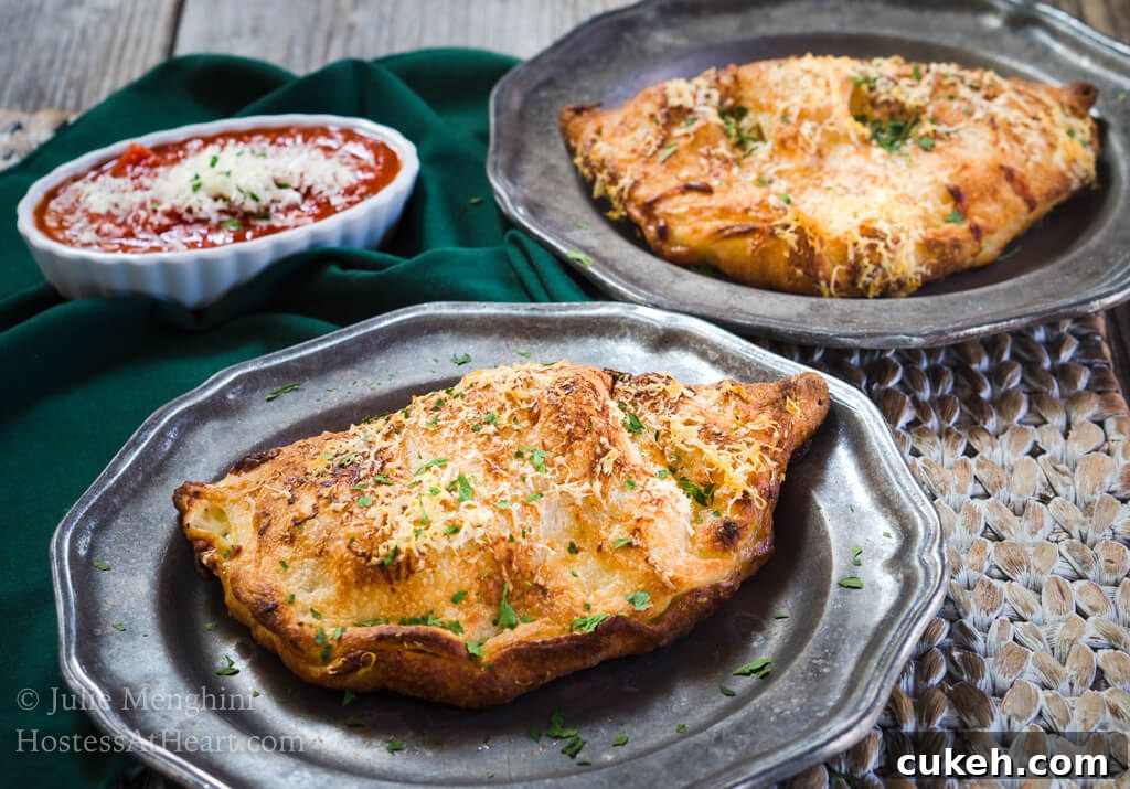 64 Tasty Leftover Ham Recipes for Every Meal 14 Ham and 3 Cheese Calzone sitting on a metal plate with a dish of marinara in the background