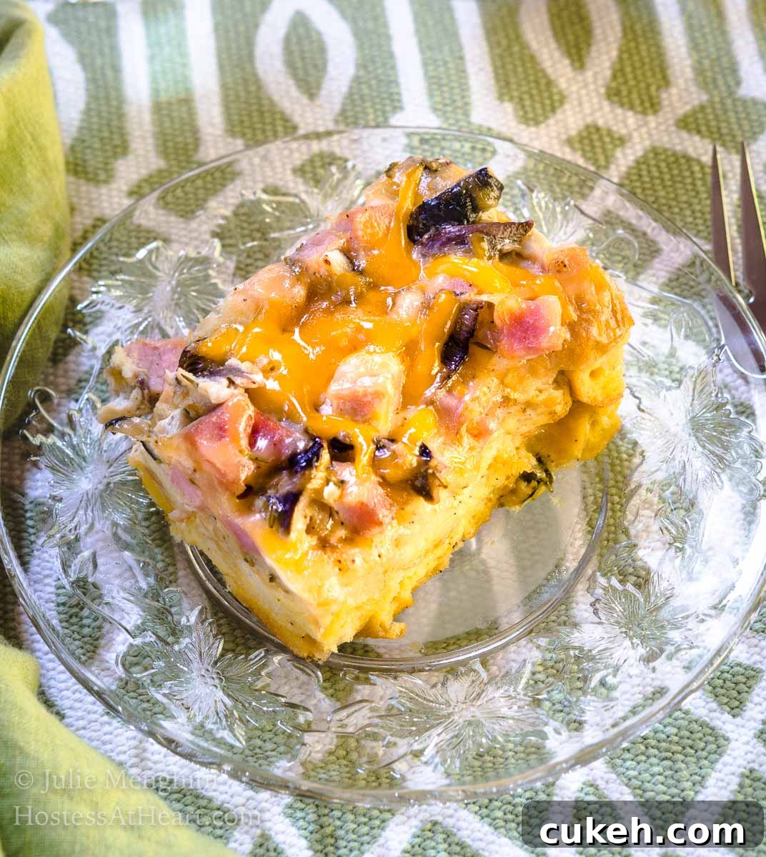 64 Tasty Leftover Ham Recipes for Every Meal 9 Top-down view of a piece of Ham and Cheese strata with melted cheese and mushrooms sitting on a clear glass plate over a green and white placemat.