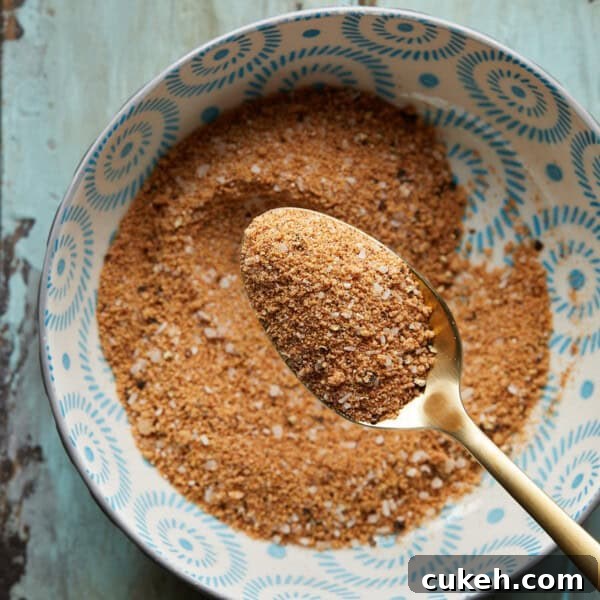 Overhead photo of a bowl of burger seasoning with a gold metal spoon on a rustic surface.