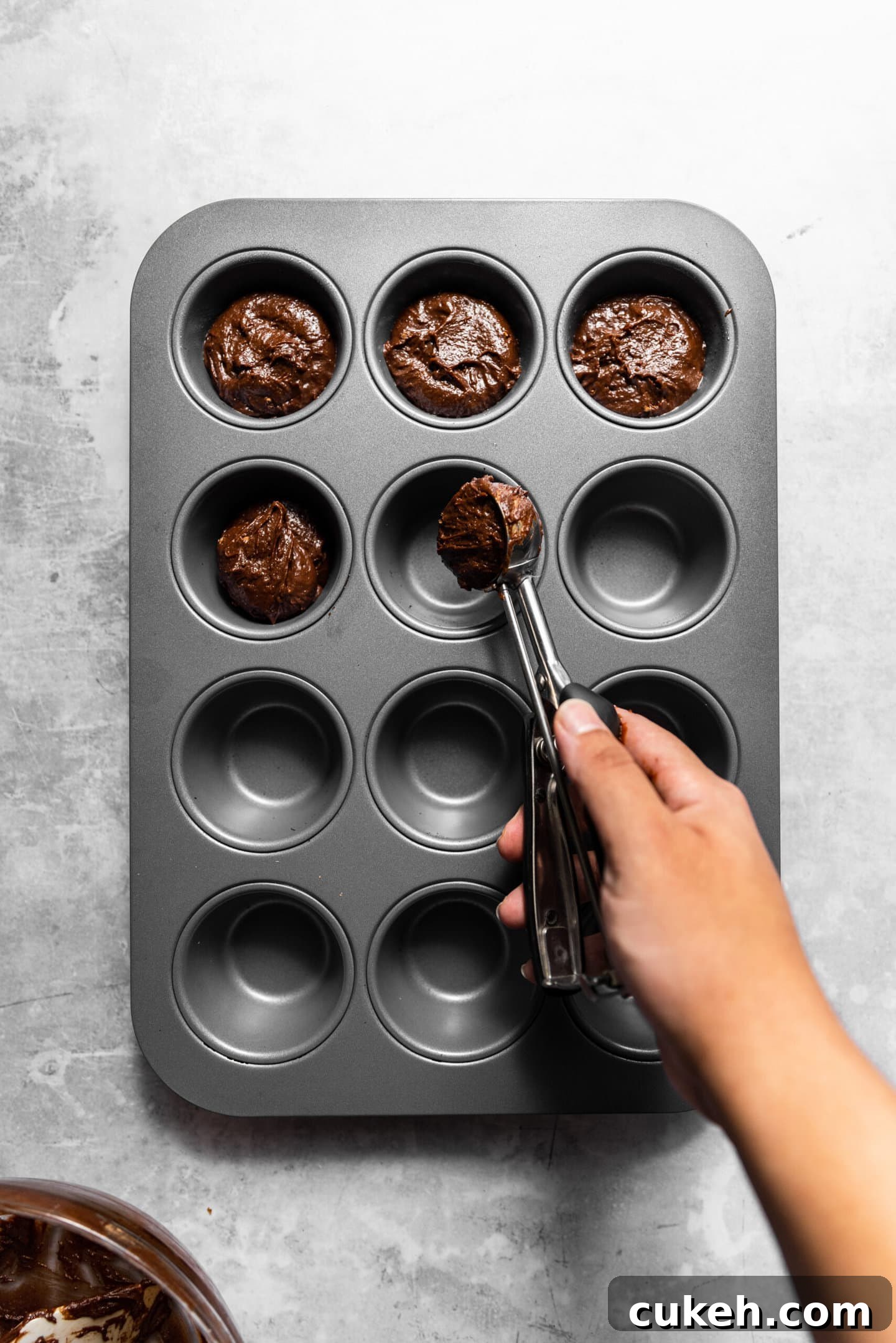 Brownie batter being scooped into muffin pan.