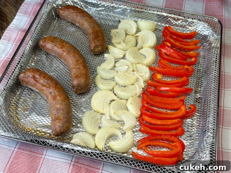 Air fryer basket with cooked sweet Italian sausage and bell peppers on a red and white plaid napkin.