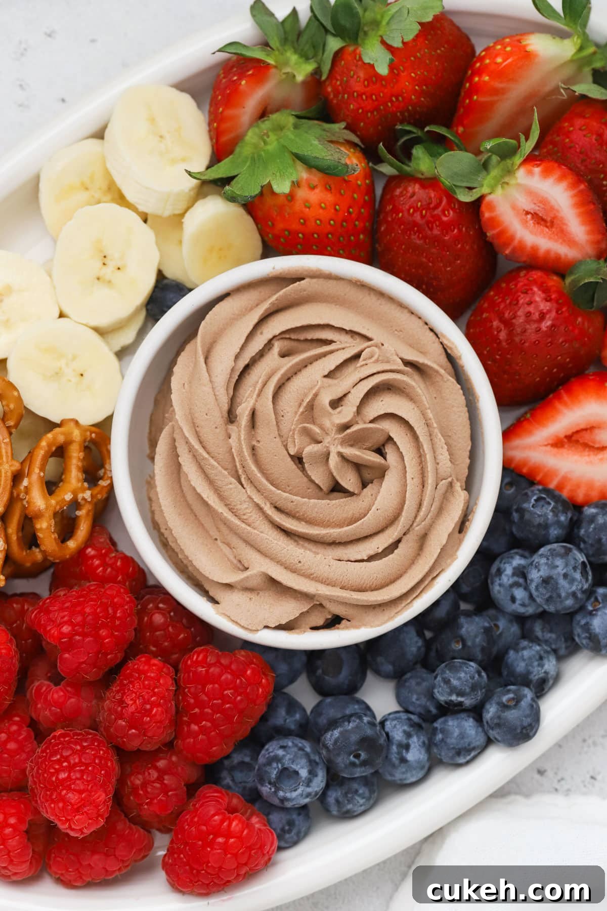 A bowl of chocolate whipped cream surrounded by colorful fresh fruit