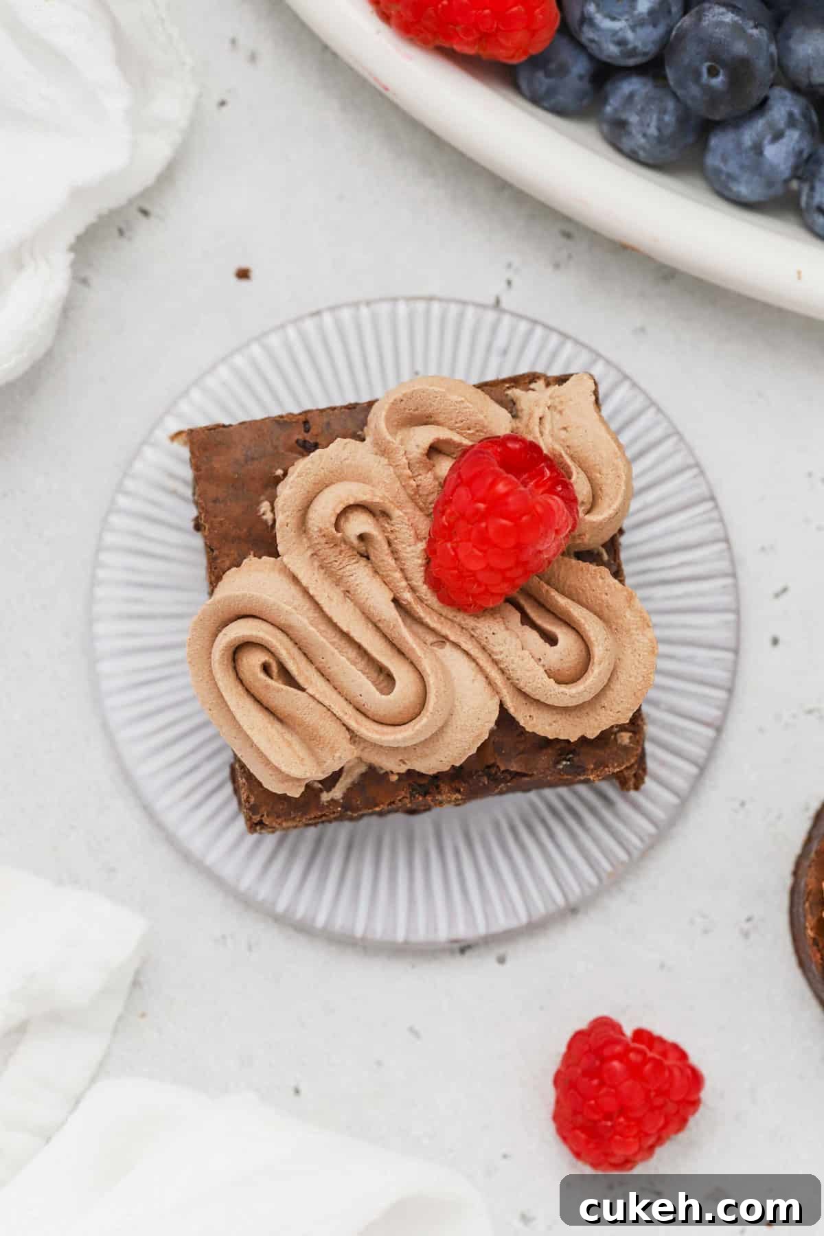 A brownie square topped with chocolate whipped cream and a fresh raspberry