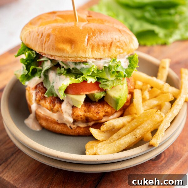 A shrimp burger on a plate with fries on a tabletop.