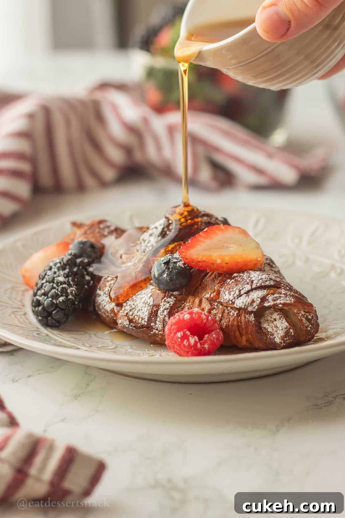 Pouring syrup over baked croissant french toast on plate.