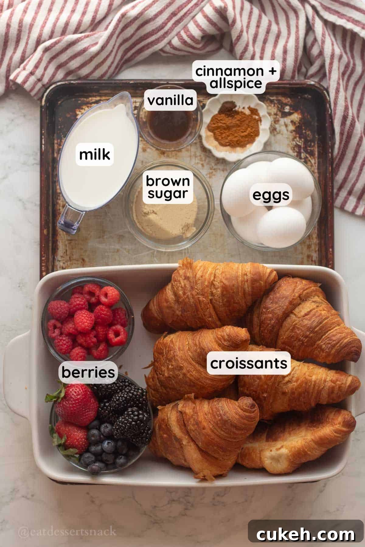 Labeled ingredients for french toast croissant casserole in bowls on metal baking tray.