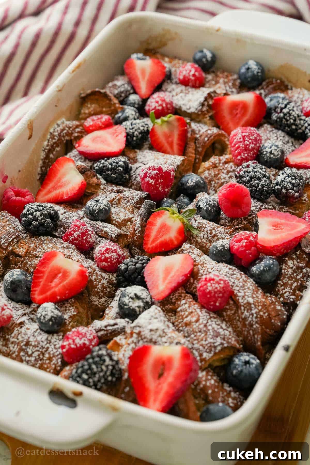 Berries and powdered sugar over french toast croissant bake in pan.