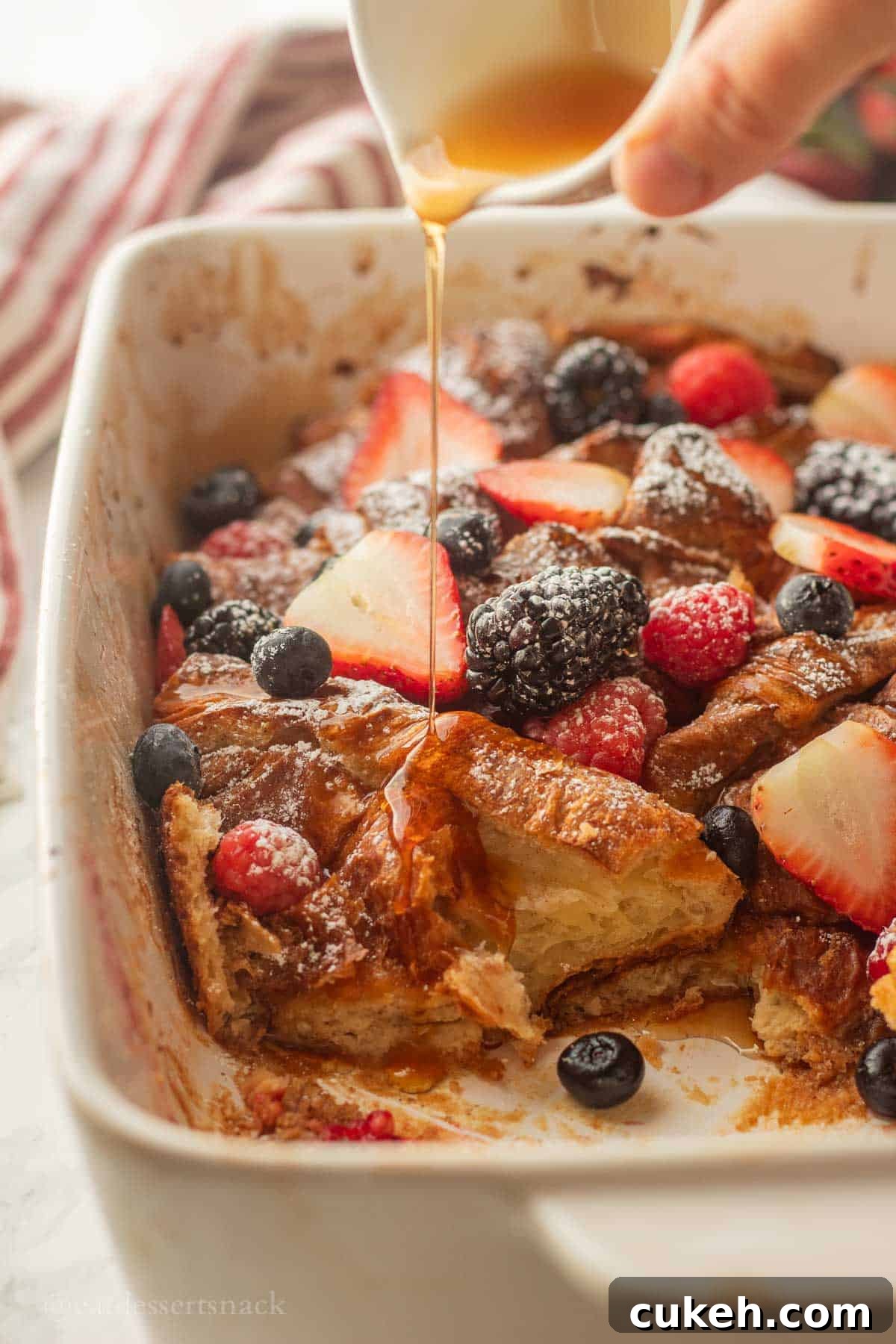 Pouring syrup over baked french toast croissants in pan.