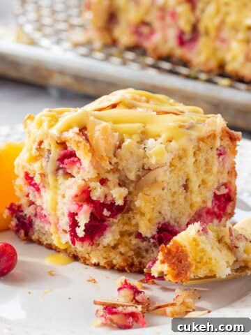 Baked cranberry orange coffee cake with bite removed on white plate.