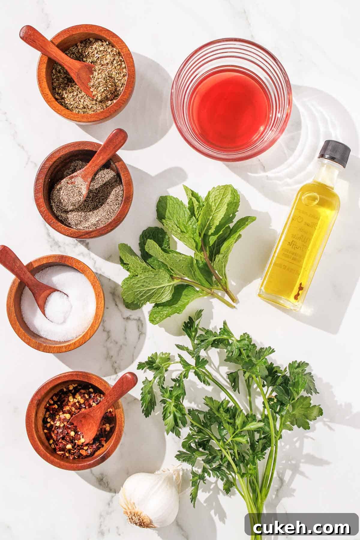 Fresh Mint Chimichurri Sauce Recipe for Grilled Meats & Veggies 3 Overhead view of various cooking ingredients including herbs, spices, olive oil, and vinegar arranged neatly on a marble surface.