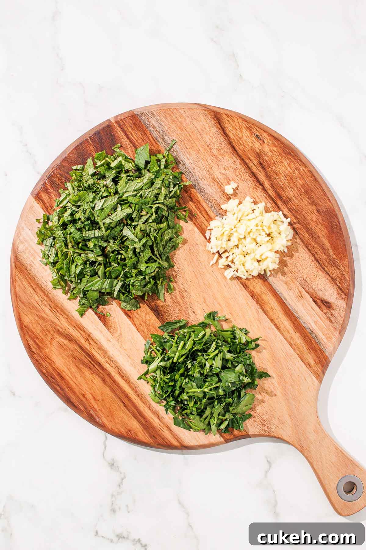 Fresh Mint Chimichurri Sauce Recipe for Grilled Meats & Veggies 4 Minced garlic and chopped herbs on a wooden cutting board.