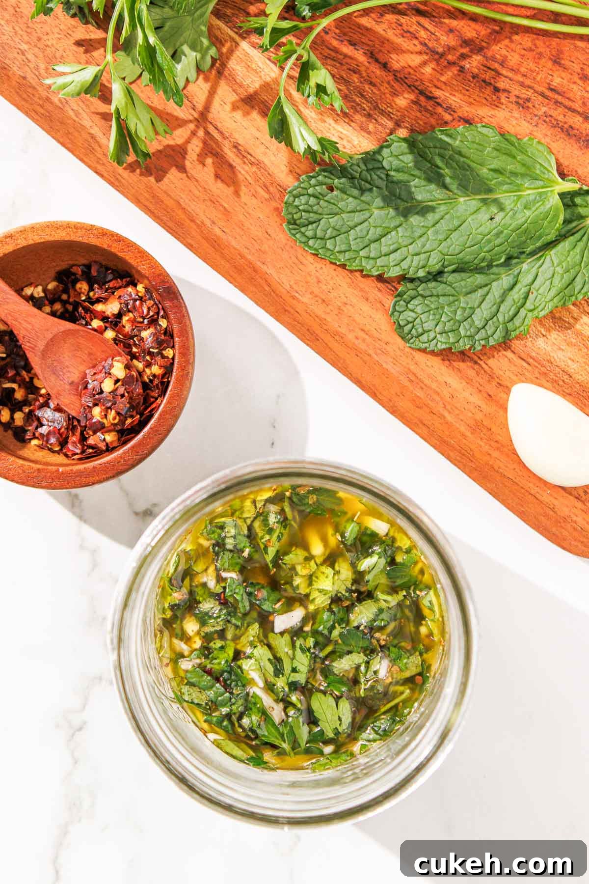 Fresh Mint Chimichurri Sauce Recipe for Grilled Meats & Veggies 7 Overhead view of a homemade mint chimichurri in a glass jar, with spices in a wooden bowl and fresh herbs on a cutting board nearby.