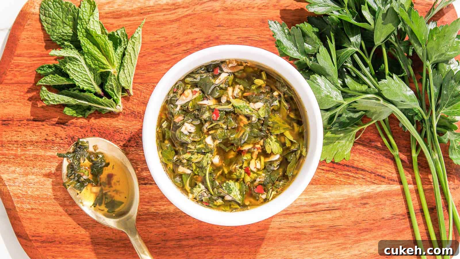 Fresh Mint Chimichurri Sauce Recipe for Grilled Meats & Veggies 10 A bowl of mint chimichurri garnished with fresh parsley and mint leaves on a wooden board, accompanied by a spoon.