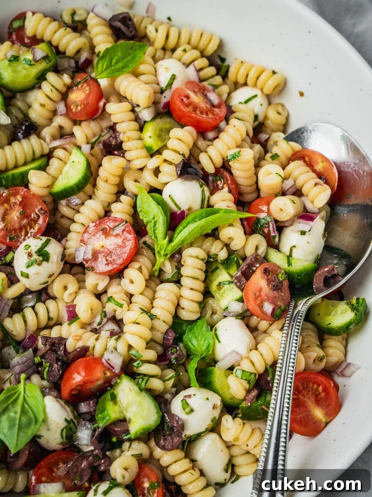Mediterranean pasta salad with cherry tomatoes, cucumber, mozzarella balls, and olives in a large serving bowl.