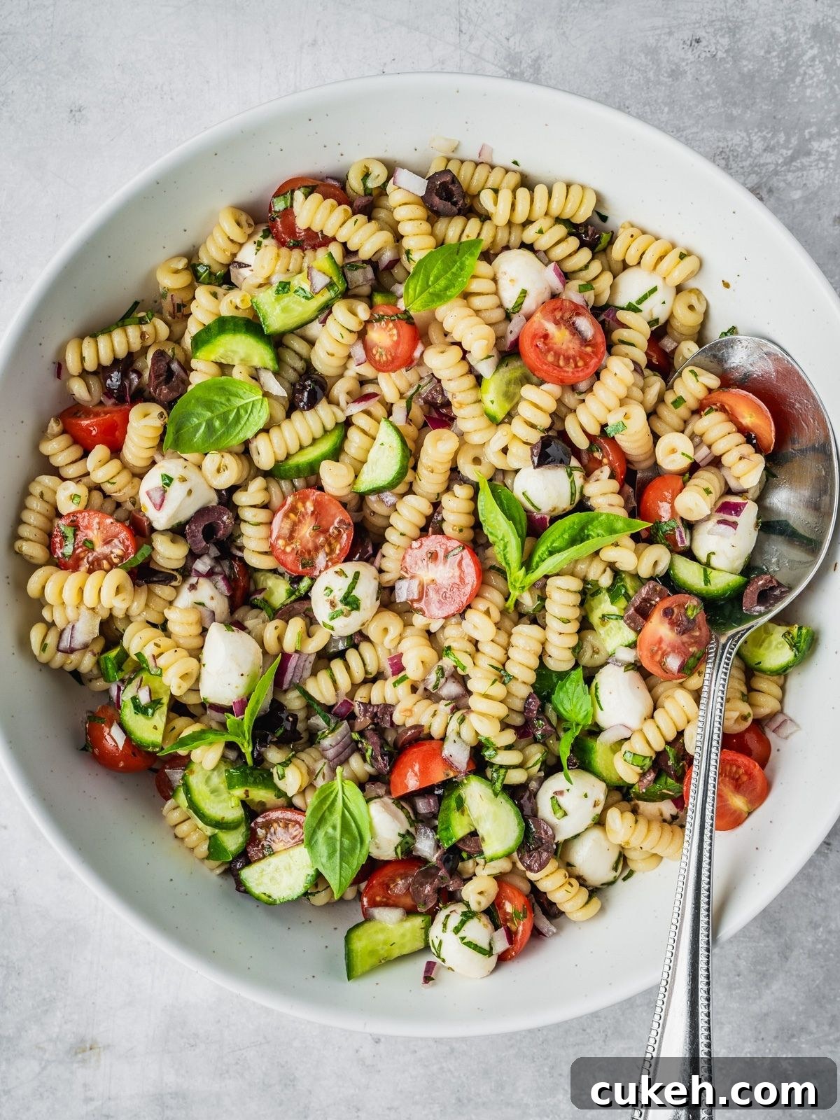 Mediterranean pasta salad with cherry tomatoes, cucumber, mozzarella balls, and olives in a large serving bowl.