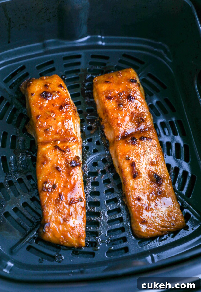 2 chipotle maple air fried salmon fillets sitting in an air fryer basket with crispy edges
