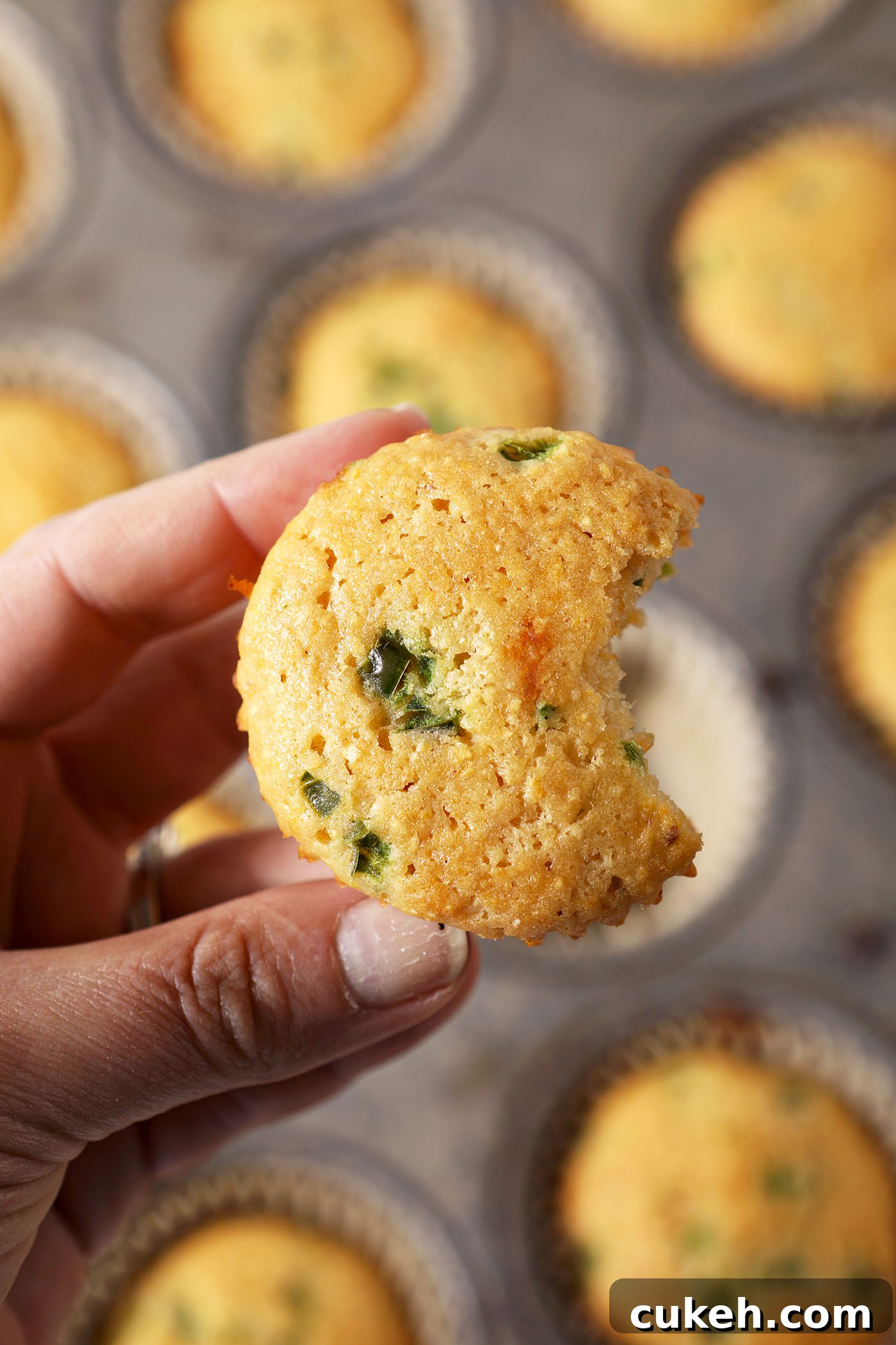 Honey Jalapeño Cornbread Muffins That Balance Sweet and Heat 2 A bitten-into Jalapeno Corn Muffin held above a muffin tin with more muffins