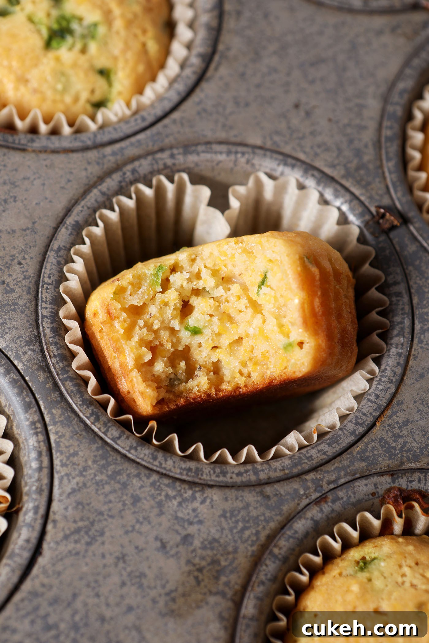 Honey Jalapeño Cornbread Muffins That Balance Sweet and Heat 7 A bitten-into Honey Jalapeno Cornbread Muffin in a tin next to other corn muffins