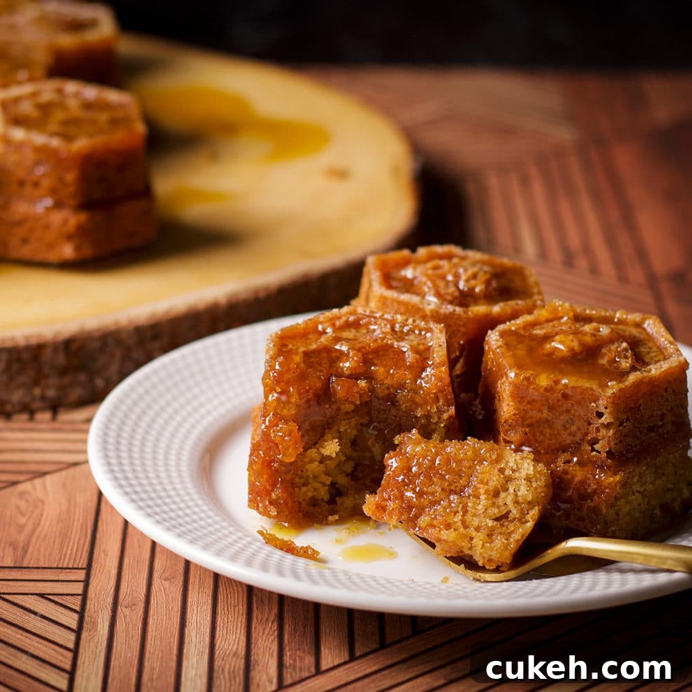 Three small pieces of honey cake baked in a honeycomb pan on a plate, with a fork taking a bite of one of the pieces of cake.