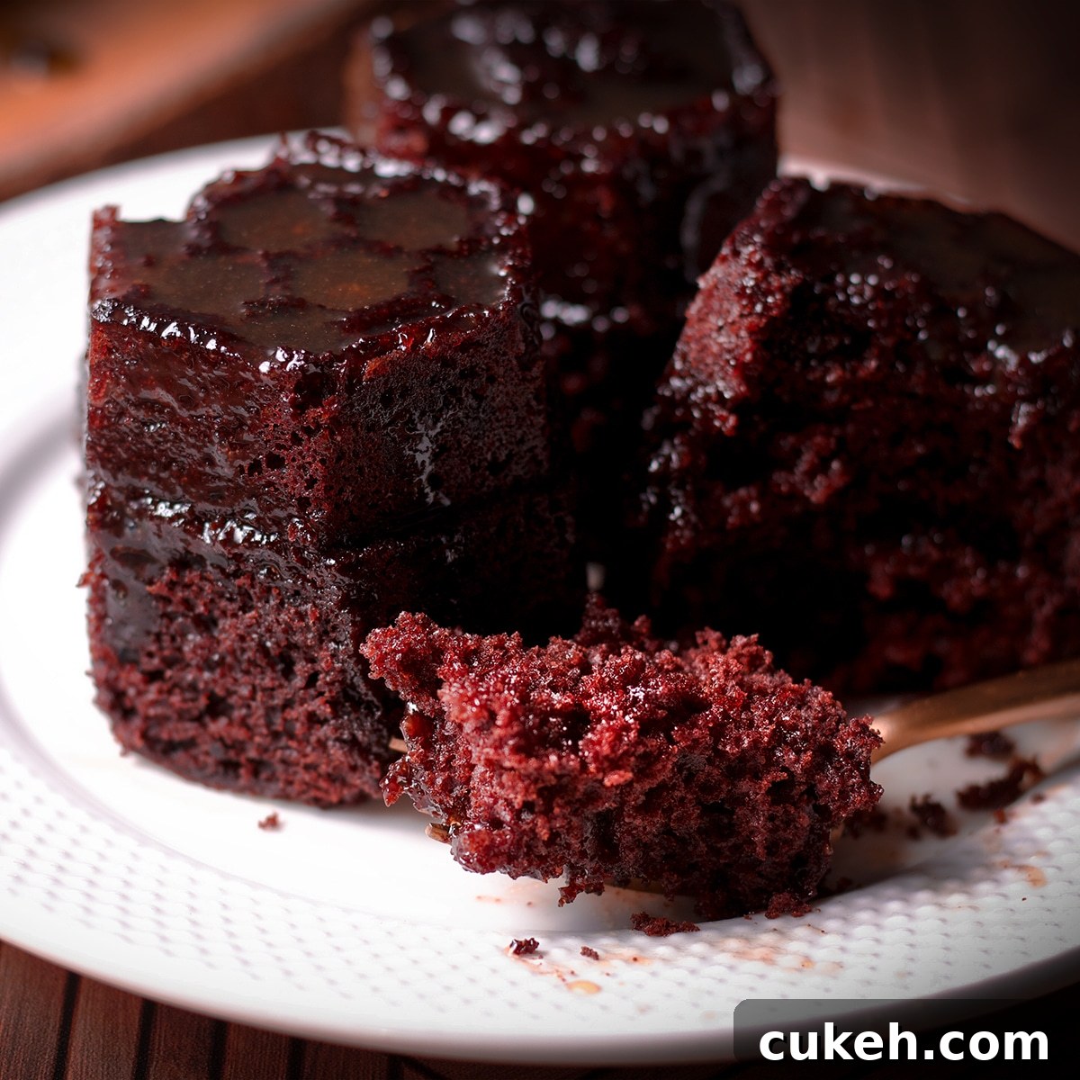 A serving of chocolate honey cake on a white plate. Someone has used a fork to cut into the cake so you can see the cake's soft texture.