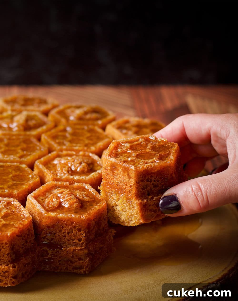 Someone taking a piece of honey cake covered in whisky sauce that has been baked in a honeycomb pan.