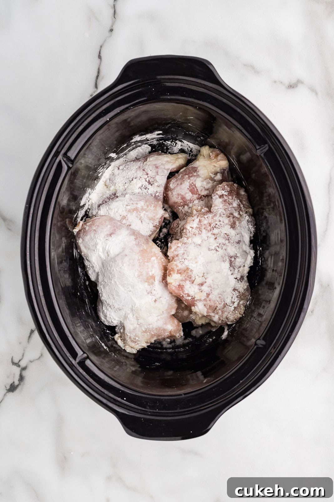 overhead view of chicken thighs in black slow cooker covered with cornstarch