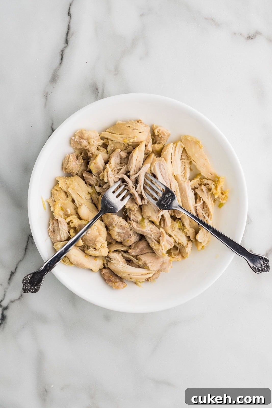 white plate with shredded chicken thighs and 2 forks