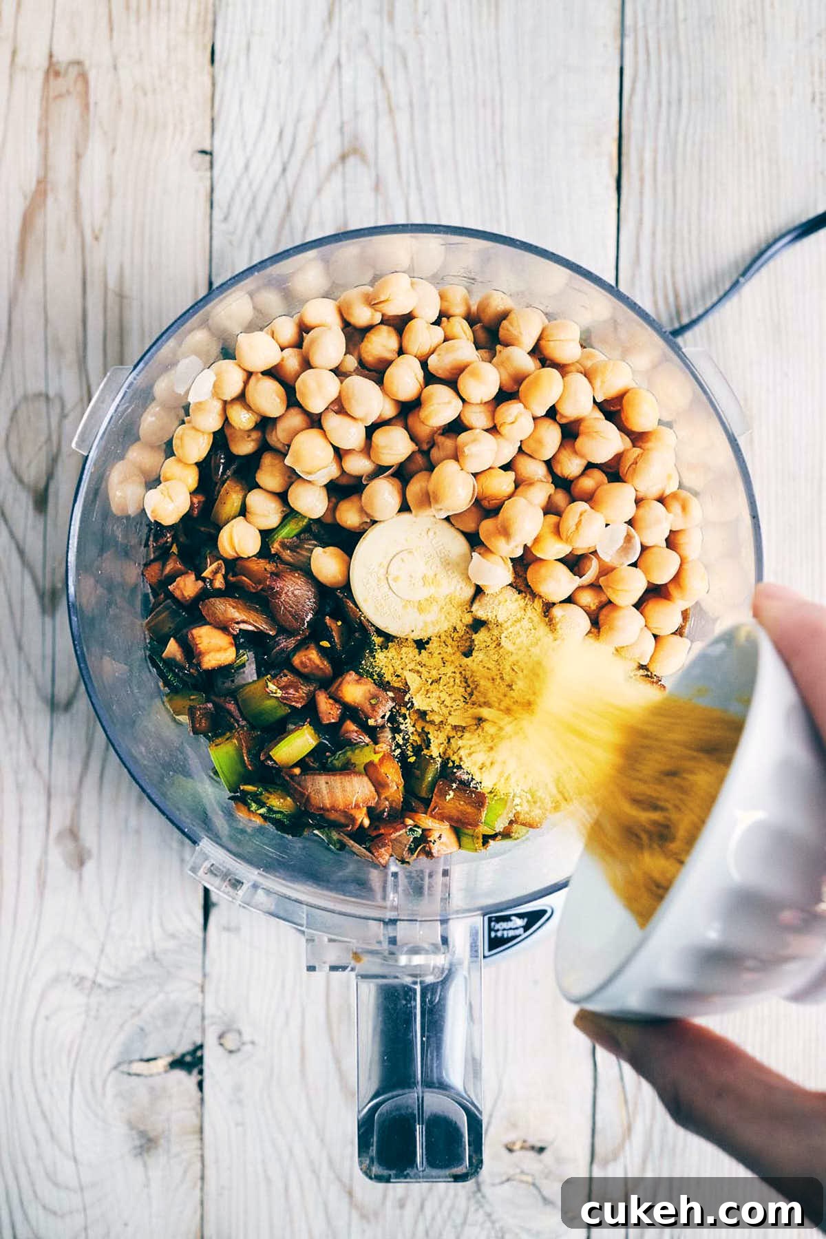 Nutritional yeast being poured into a food processor with chickpeas and cooked down mushrooms