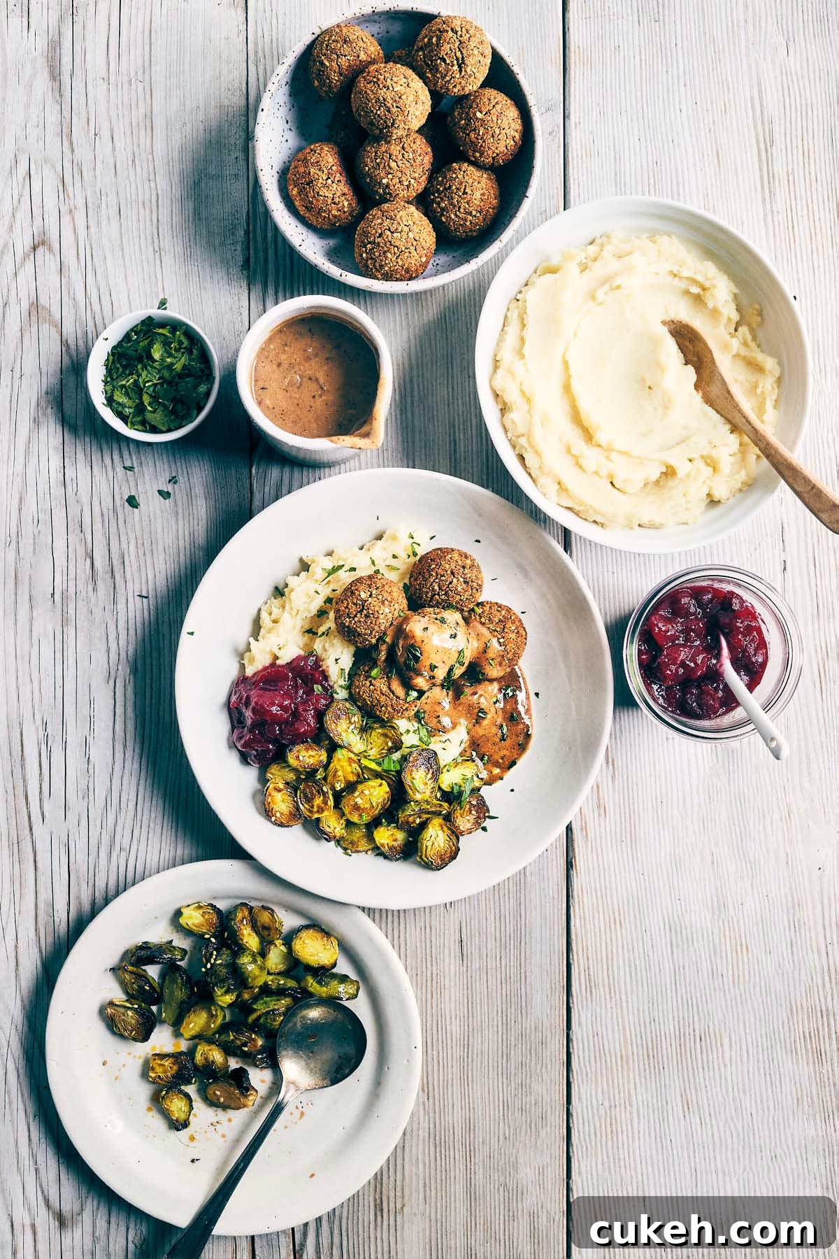 Wide table scene of vegan meatballs with mushroom miso gravy, brussels sprouts, cranberry sauce and mashed potatoes