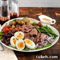Roast beef nicoise salad arranged on a platter with eggs, deli sliced roast beef, tomatoes, olives, potatoes, onions, green beans, and a Dijon mustard dressing.