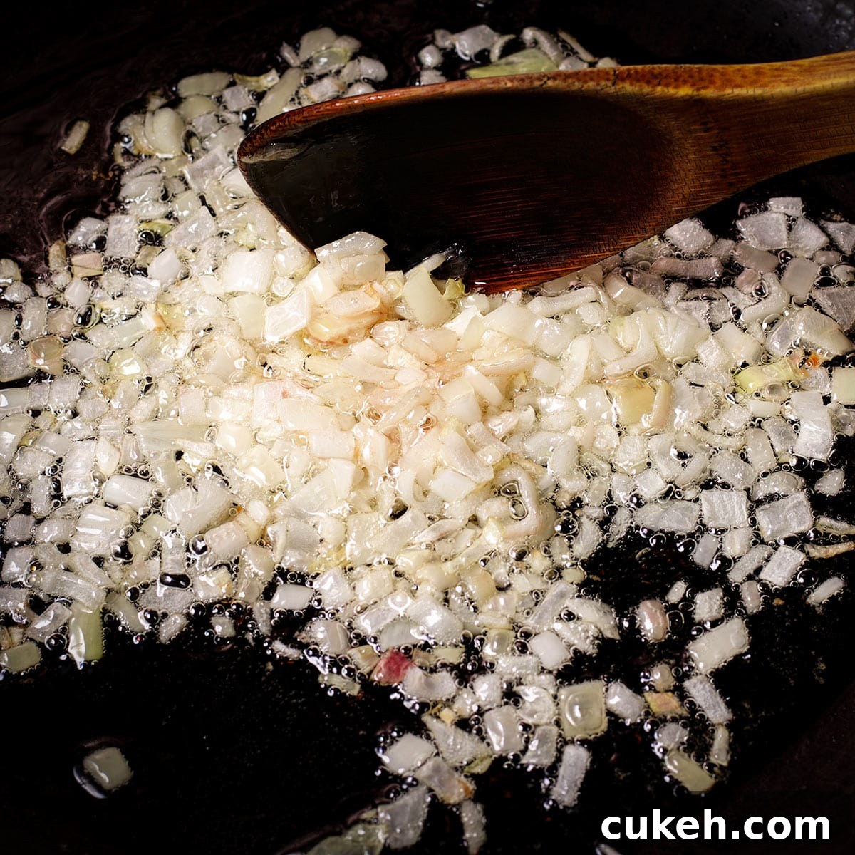 Using a spoon to stir diced shallots as they cook in olive oil in a skillet.